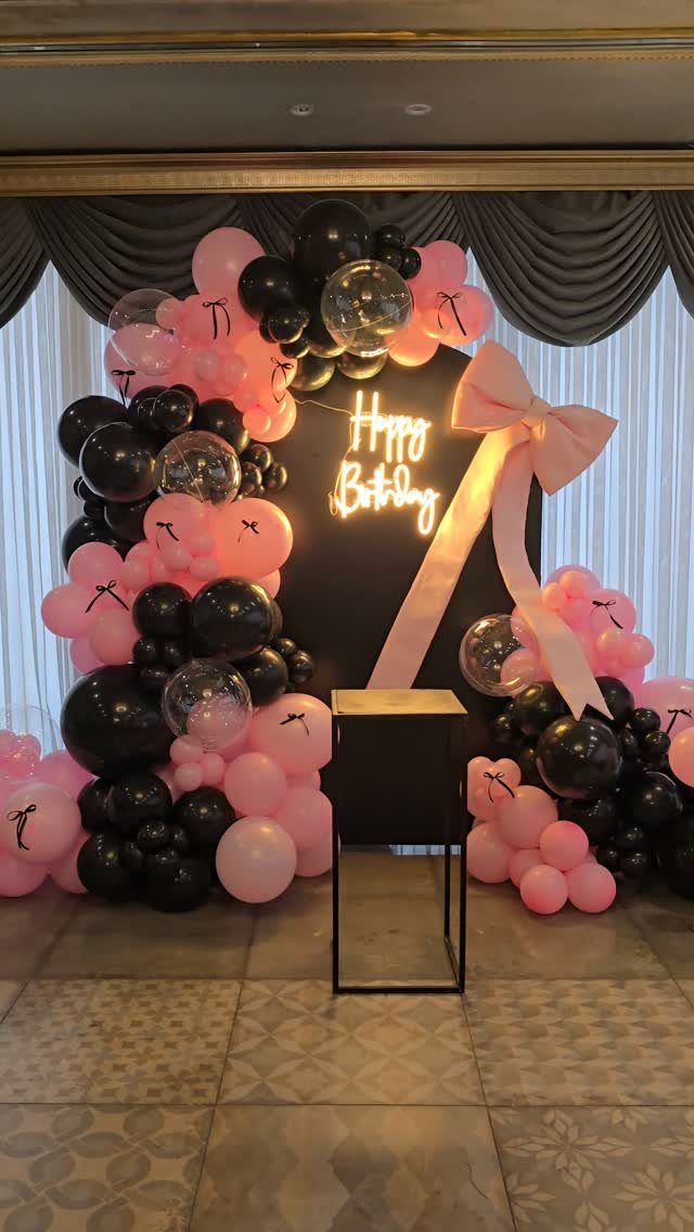 Black and pink balloon arch framing a glowing Happy Birthday neon sign backdrop.