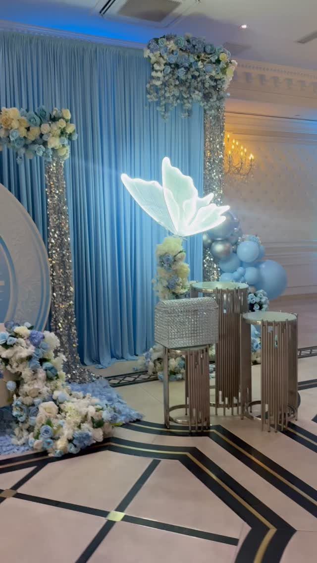 Blue and silver party decorations with floral pillars and a glowing butterfly light.