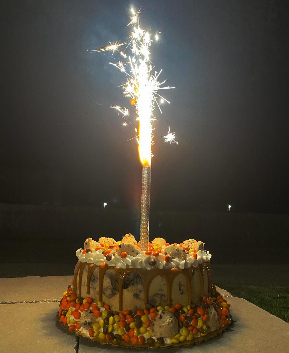 Lit sparkler candle on a decorated cake with caramel and colorful candies.