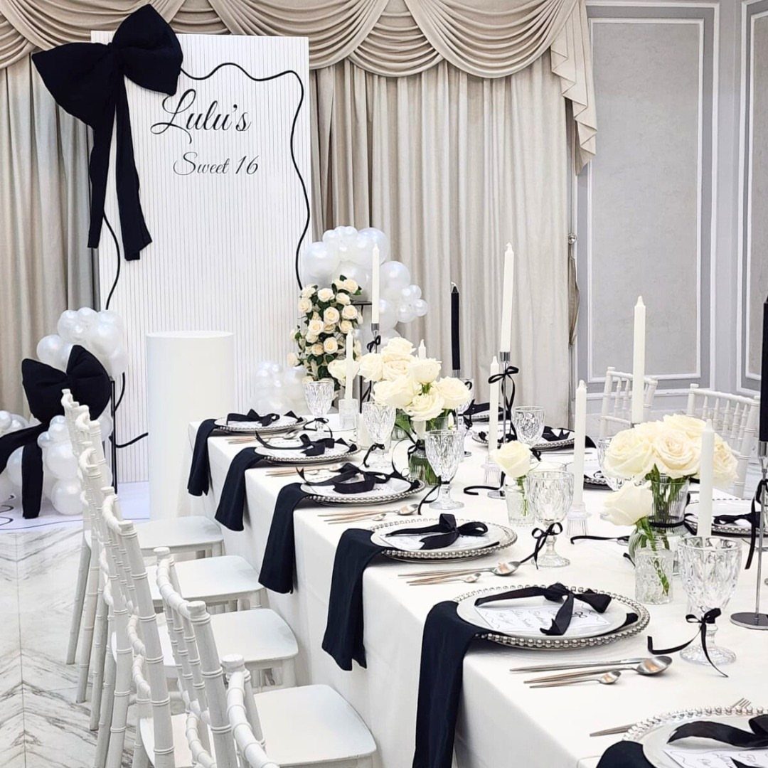 Elegant black and white party table setting with white roses and balloons.