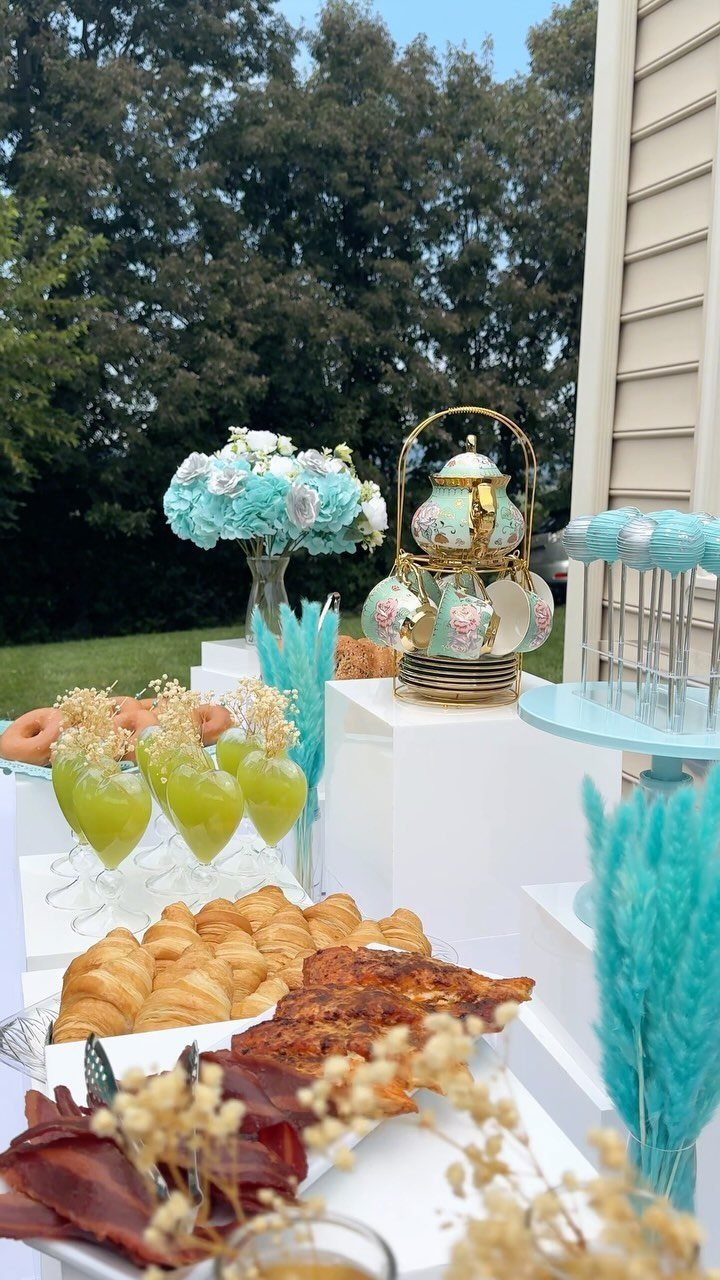 Brunch buffet with turquoise accents, pastries, and a tea set on white pedestals.