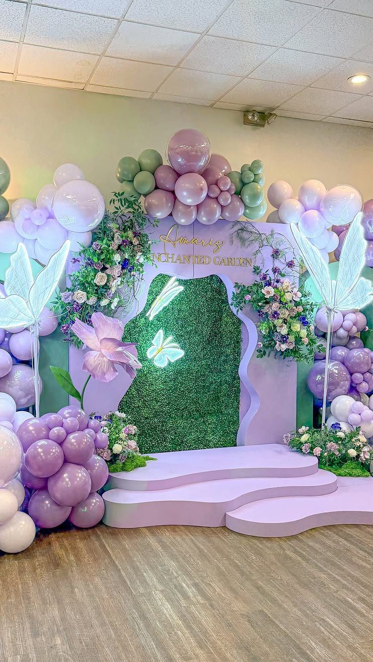 Enchanted Garden party backdrop with purple balloons, floral arches, and green hedge wall.