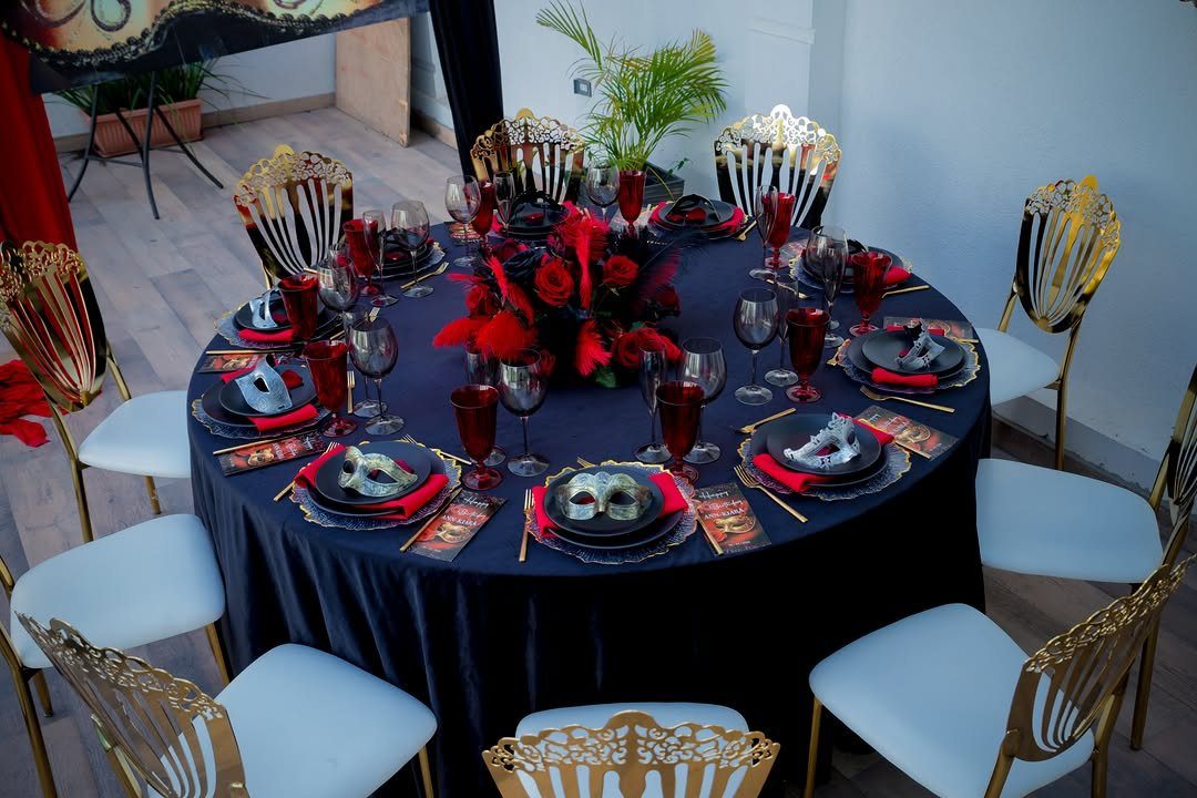Formal dinner table with black cloth, red roses, and masquerade masks at each setting.