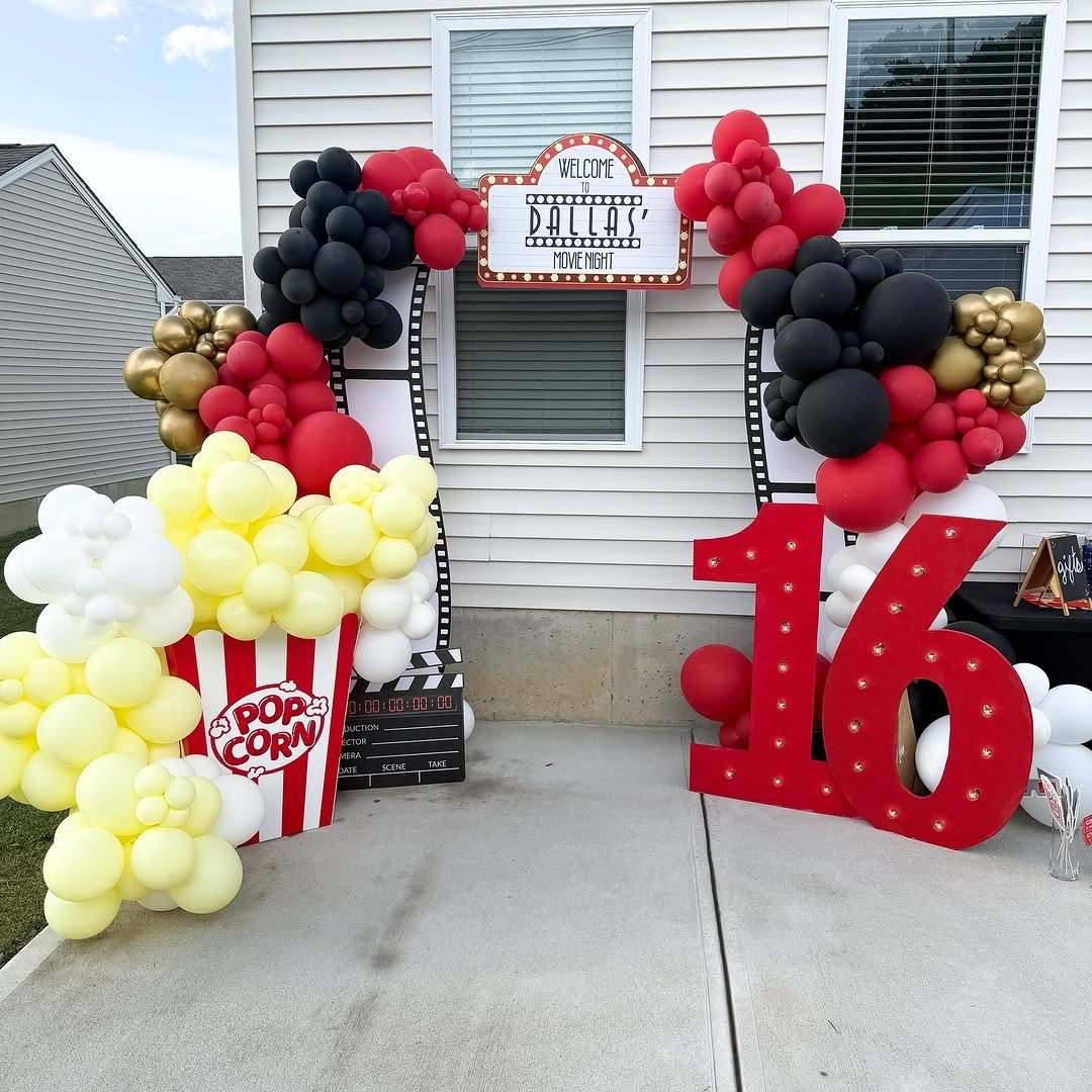 Movie themed party decorations with a balloon arch, giant popcorn, and red number 16.