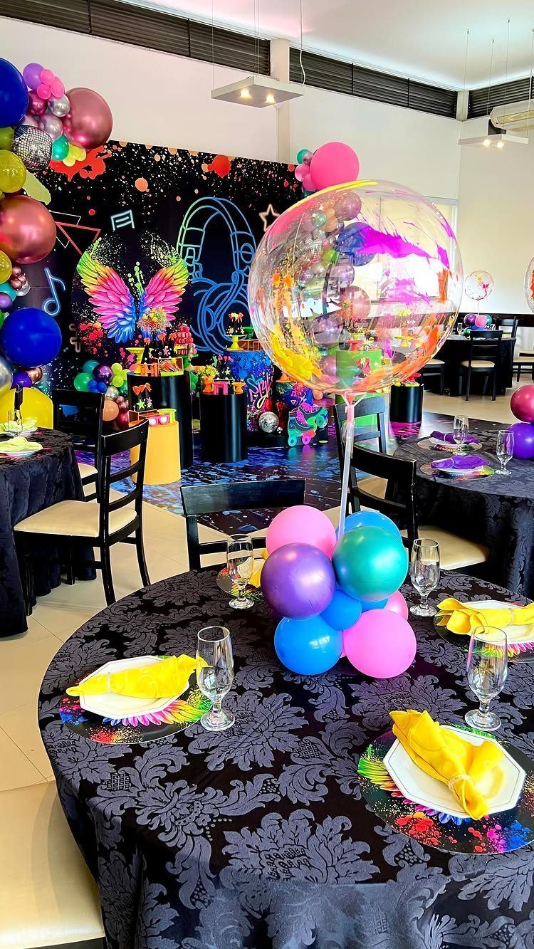 Party table with colorful balloons and a neon headphone backdrop in a room.
