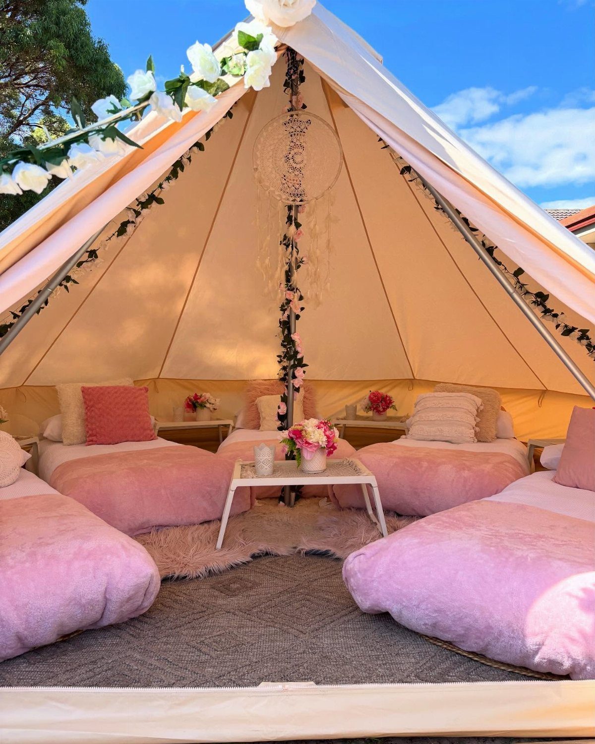 Interior of a beige bell tent with pink bedding and floral decorations.