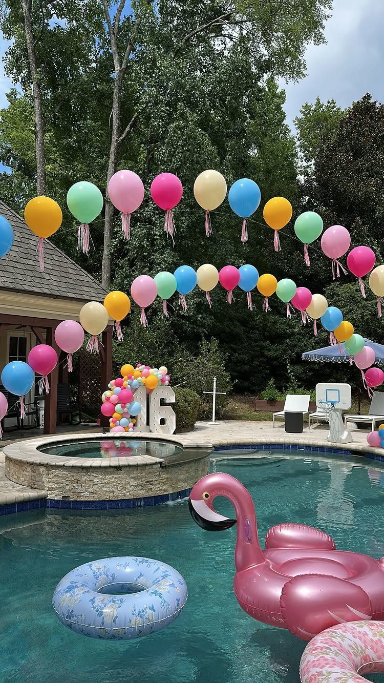 Swimming pool party setup with colorful balloon arch and pink flamingo float.