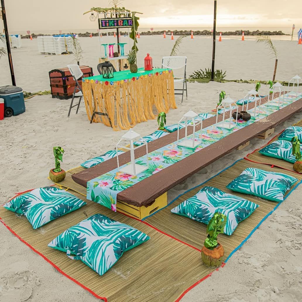 Tropical beach party setup with a tiki bar and low table with palm cushions.