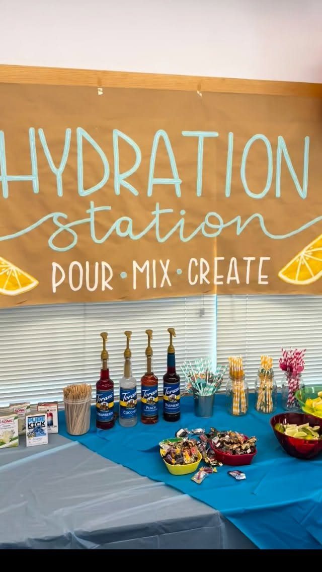 Hydration station with syrup bottles and toppings on a blue tablecloth under a banner.