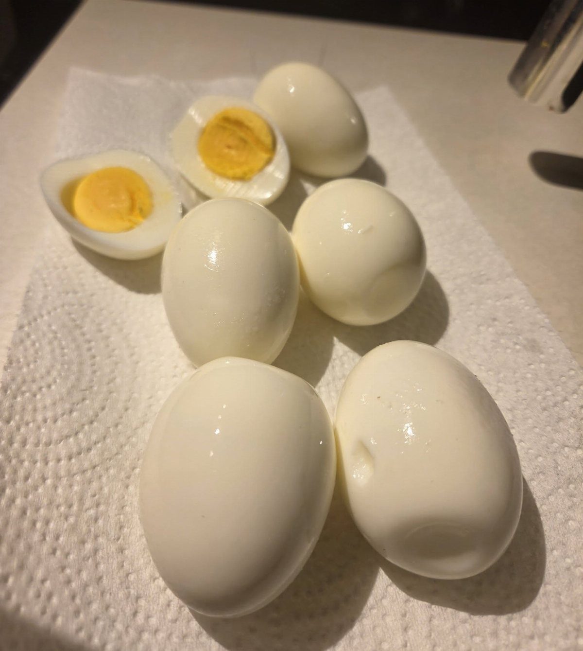 Peeled hard boiled eggs, some halved, resting on a white paper towel.