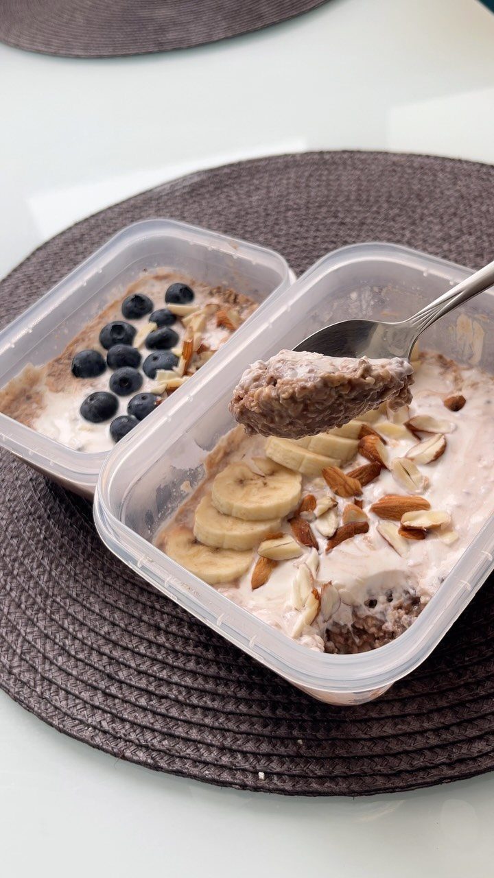 Overnight oats in plastic containers topped with blueberries, bananas, and sliced almonds.