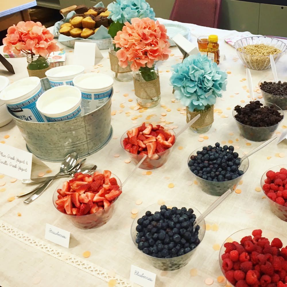 Yogurt parfait bar with fresh berries, yogurt containers, and colorful hydrangea flowers.