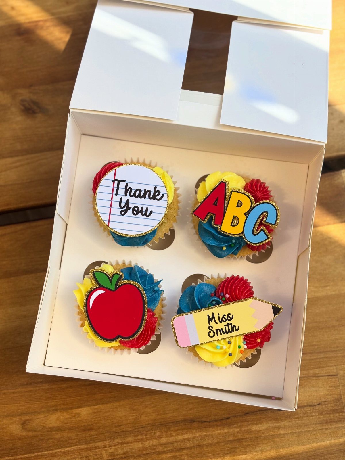 Four colorful cupcakes with school-themed toppers including a red apple and pencil.