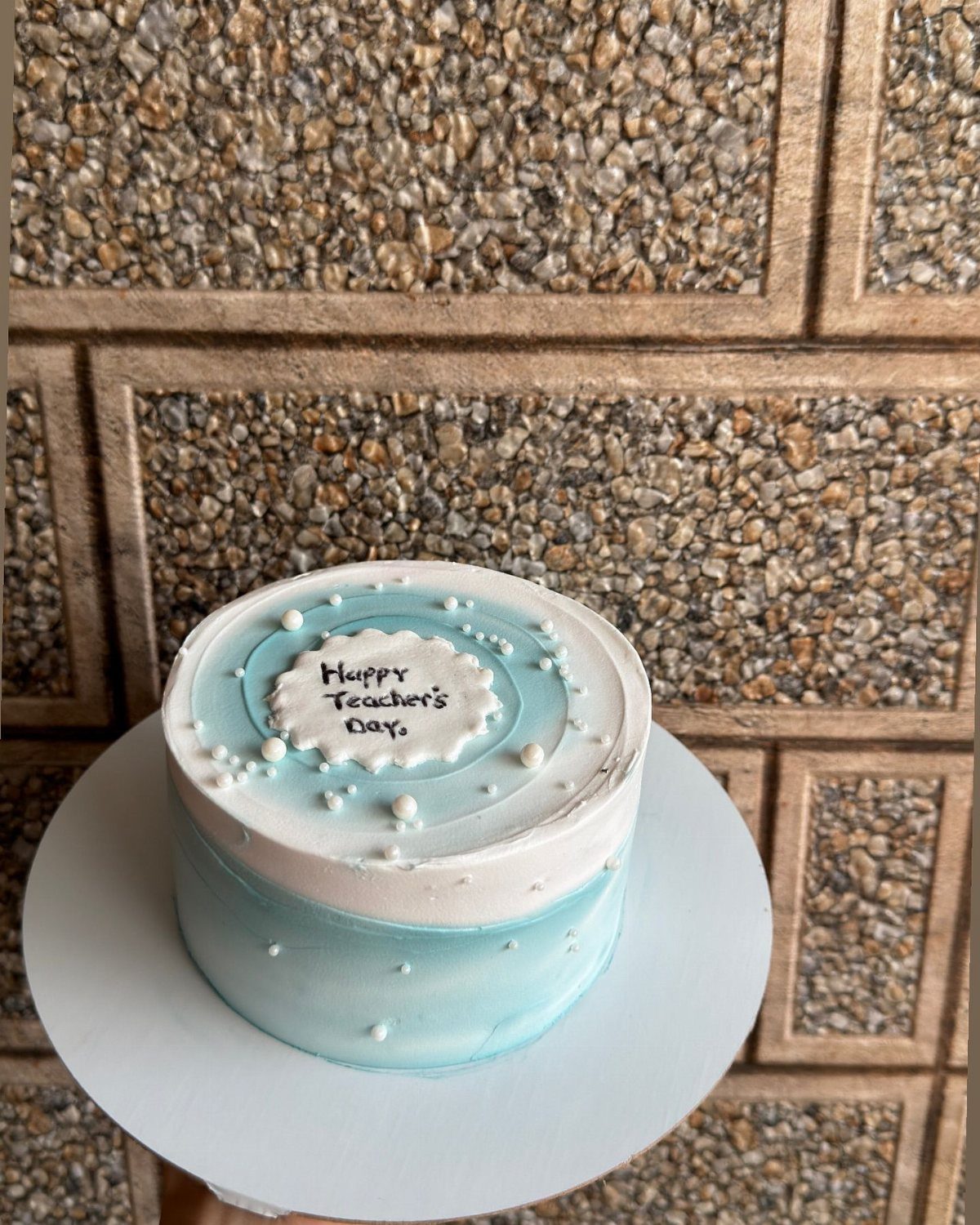 Light blue and white cake with Happy Teacher's Day plaque and pearl decorations.