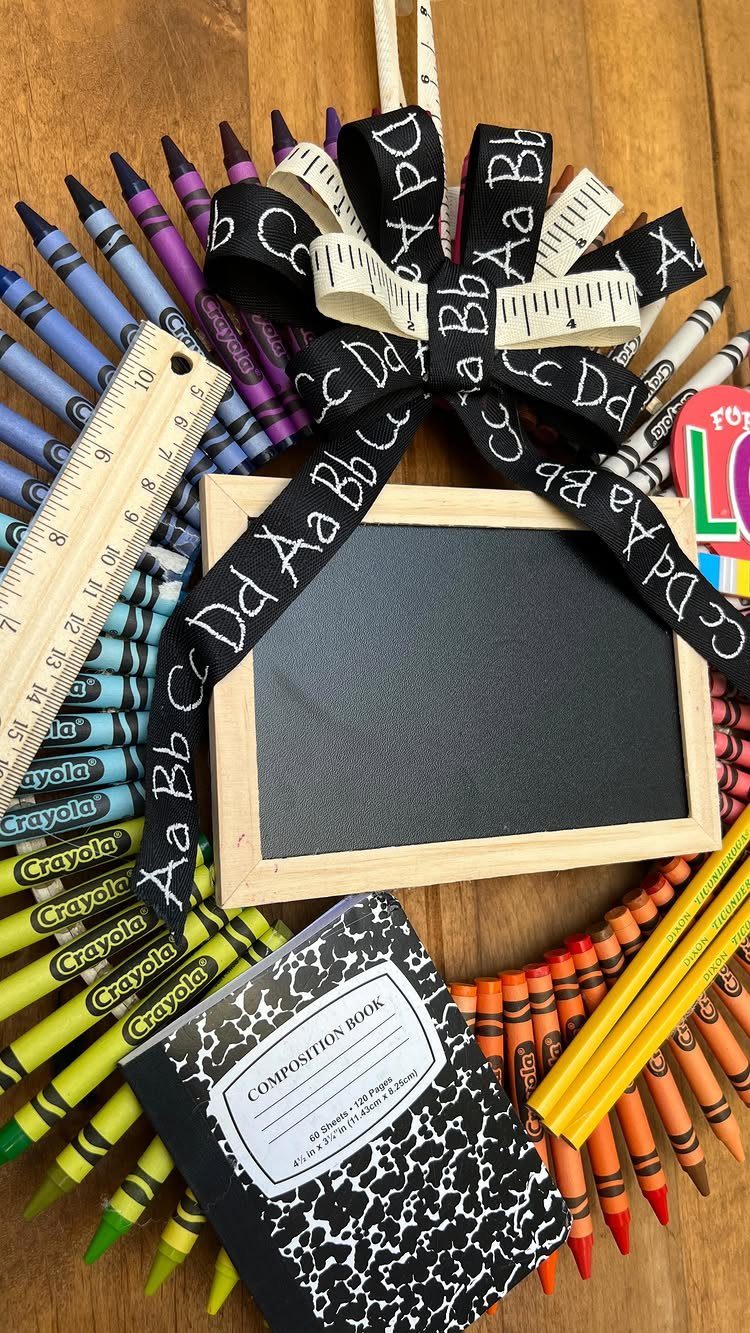 Multicolored crayon wreath with a small chalkboard, alphabet ribbon, and school supplies.