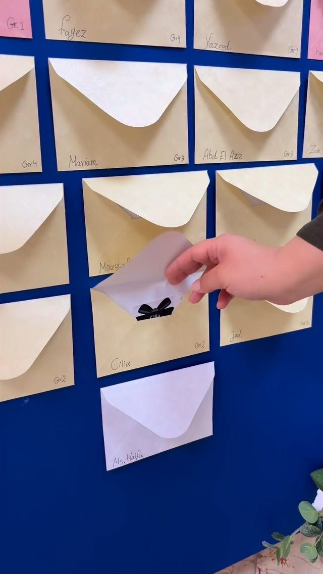 Hand placing a white envelope into a grid of envelopes on a blue wall