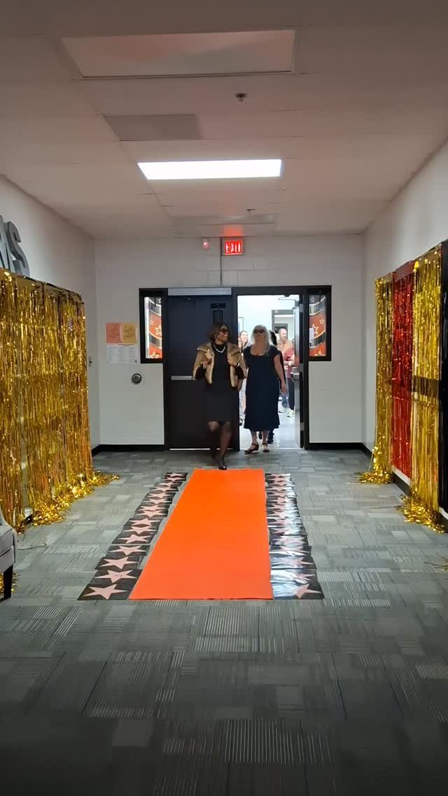 Red carpet with stars and gold foil curtains in a school hallway.