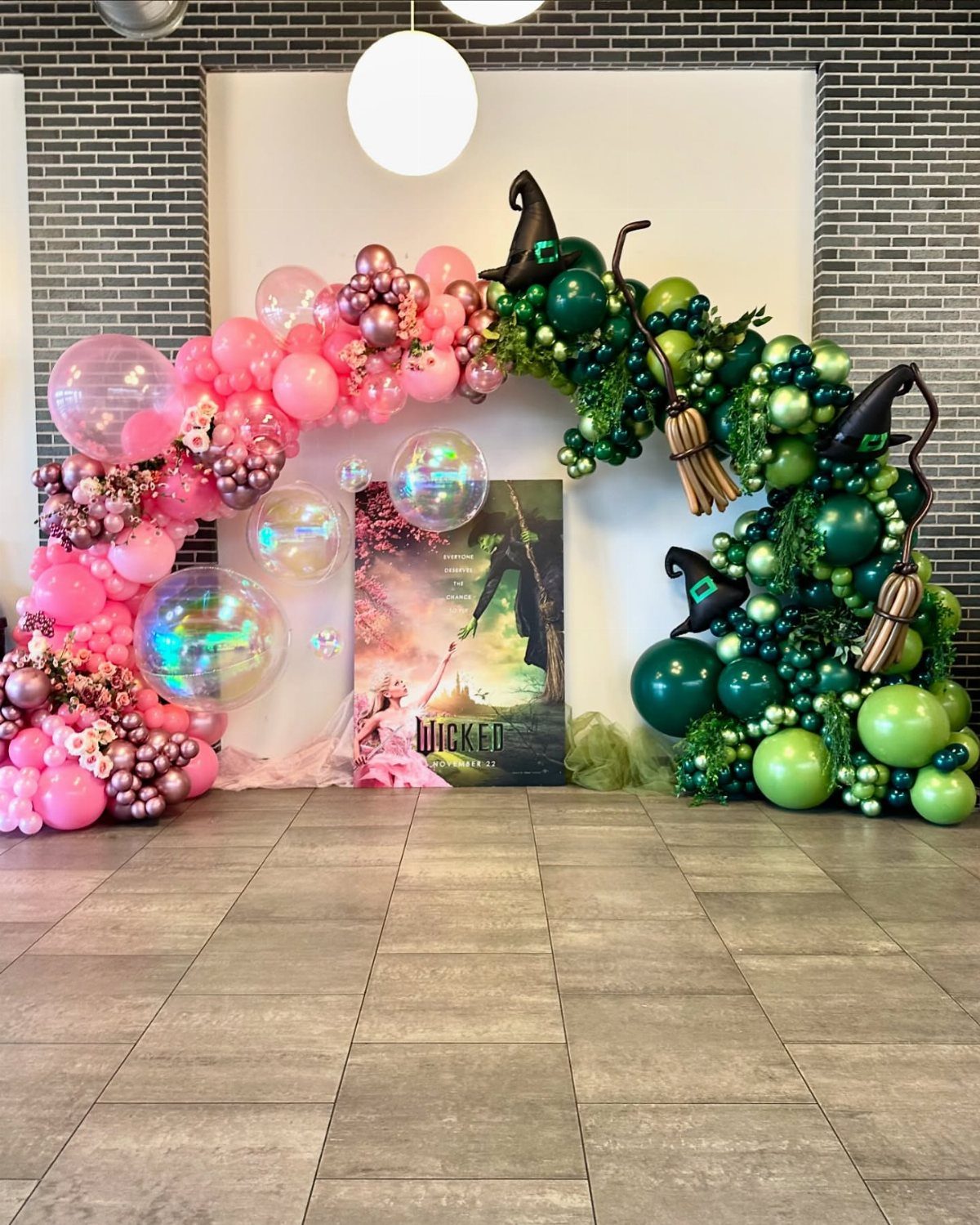 Wicked themed balloon arch with pink and green balloons, witch hats and brooms.