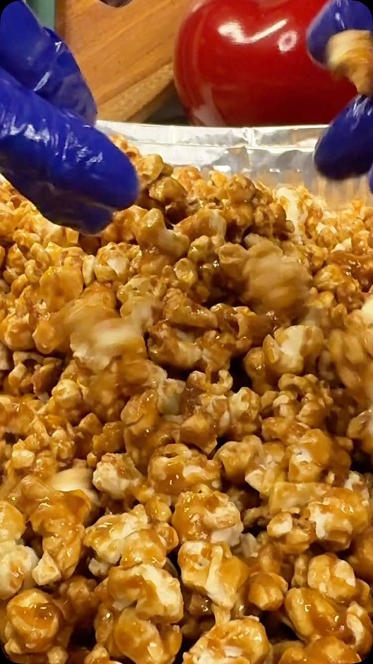 Caramel corn in a foil tray being handled by blue gloved hands.