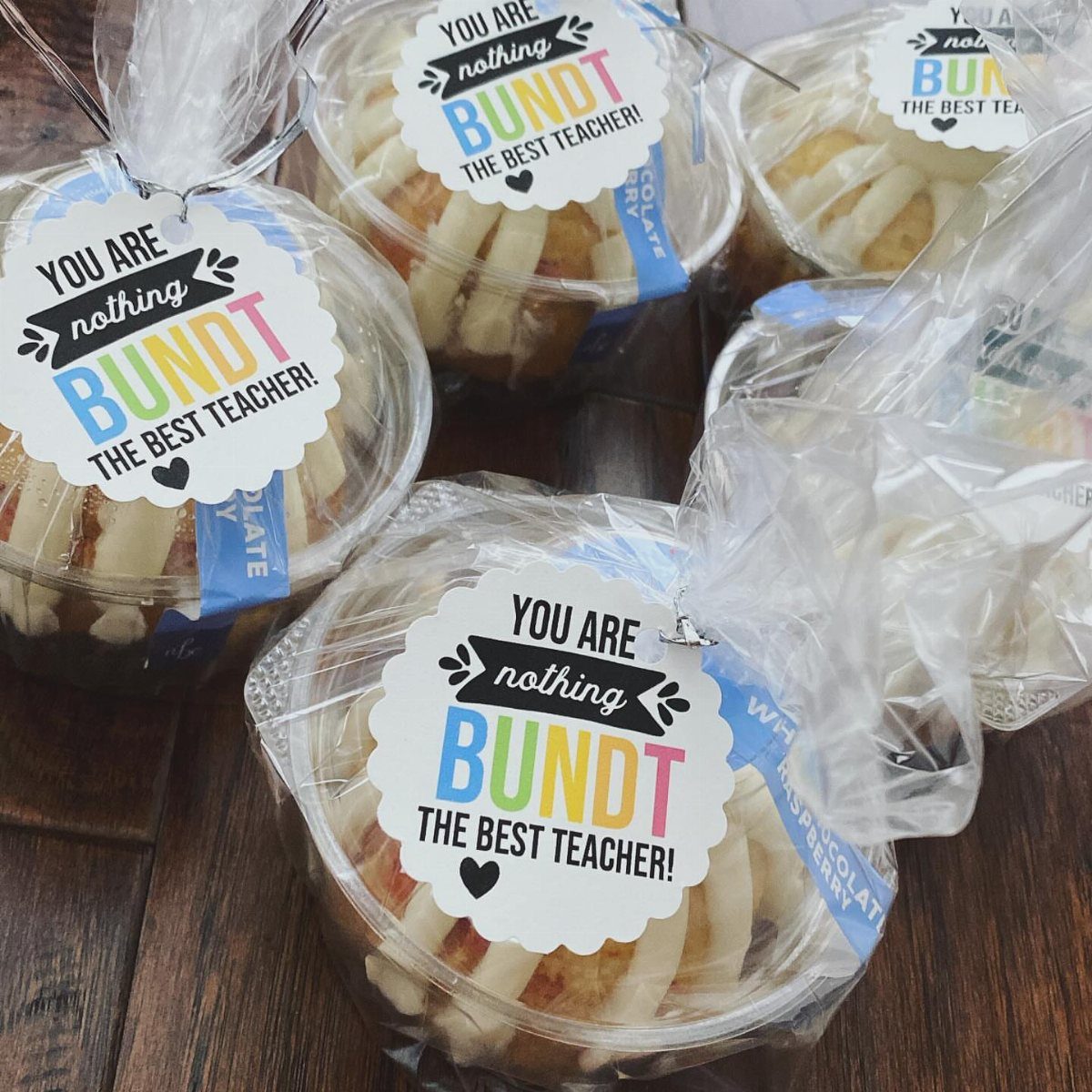 Mini bundt cakes in clear containers with teacher appreciation labels on wooden table