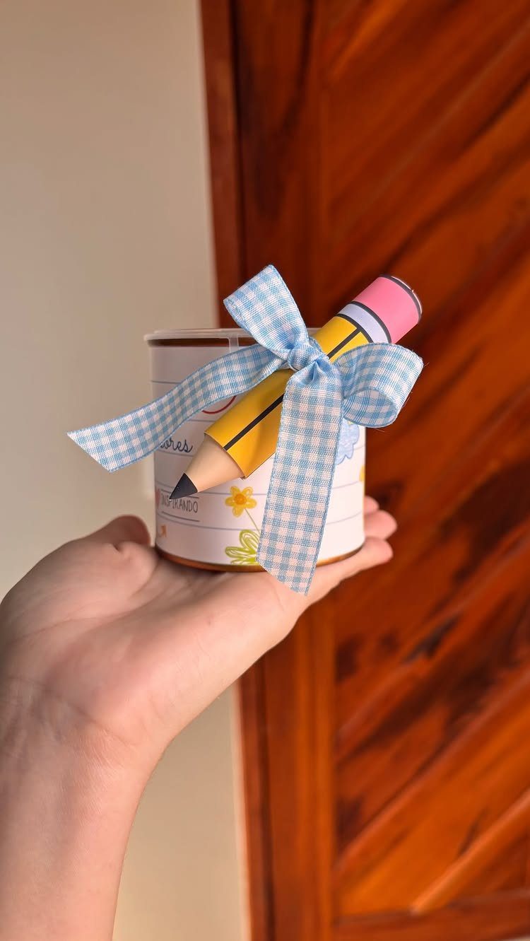Pencil-shaped cookie tied with a blue checkered ribbon inside a small white tin.
