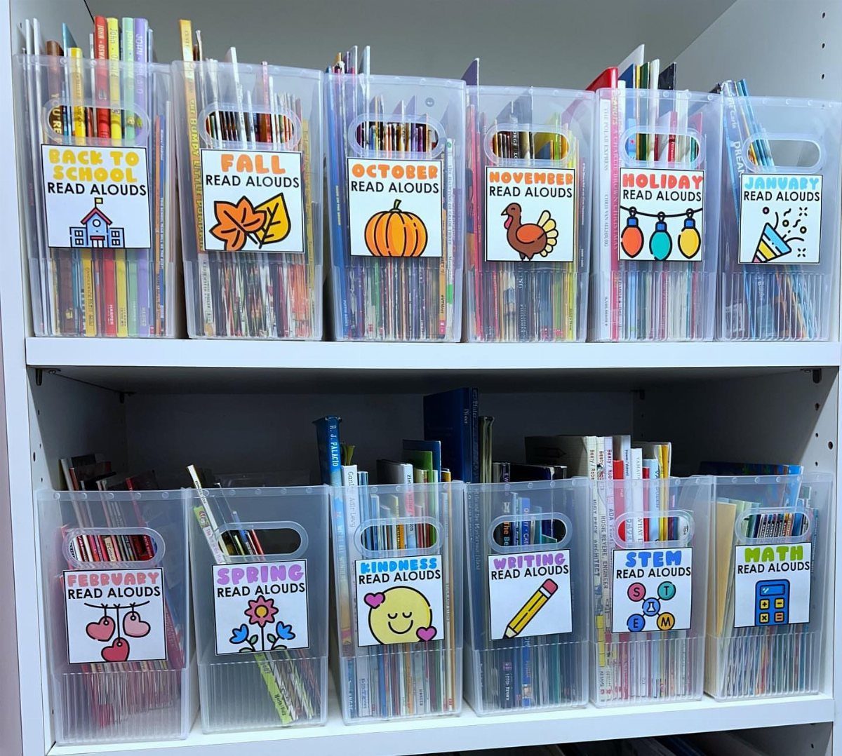 Clear plastic bins filled with colorful children's books organized by monthly themes on shelves.