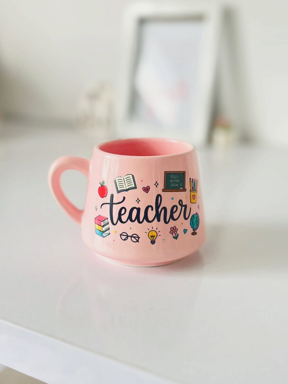 Pink ceramic coffee mug with teacher text and colorful school-themed illustrations.