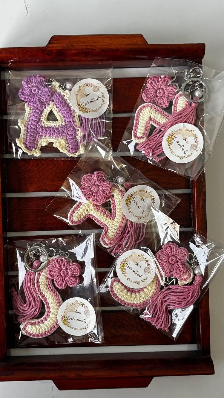 Crochet letter keychains in pink and purple wrapped in plastic on wooden tray