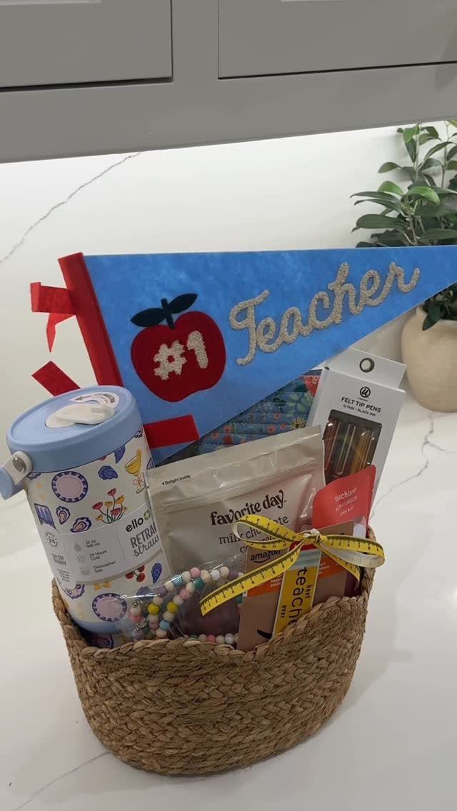 Woven gift basket containing a teacher pennant, patterned tumbler, and various small gifts.