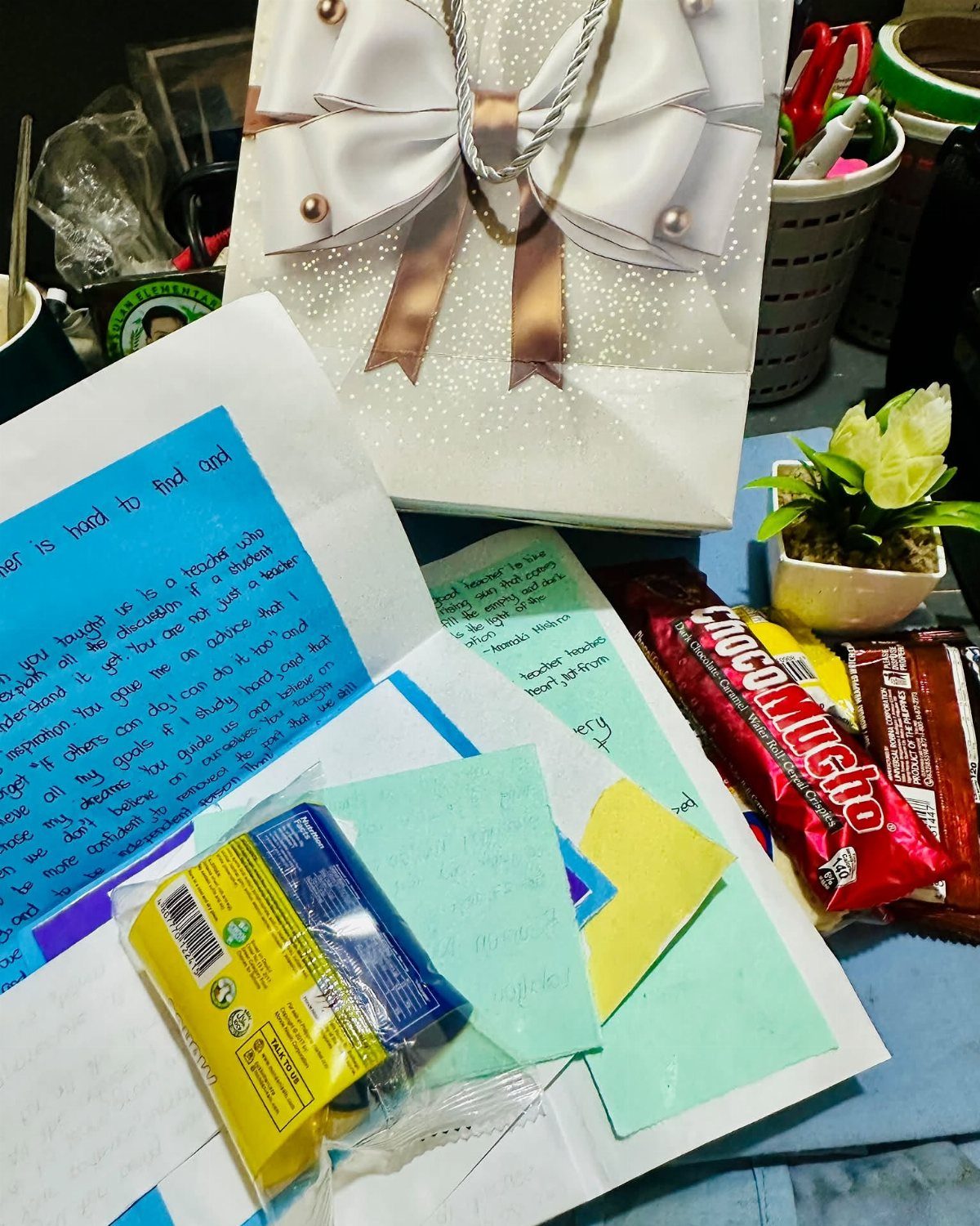 Handwritten notes and chocolates next to a white gift box and small plant.