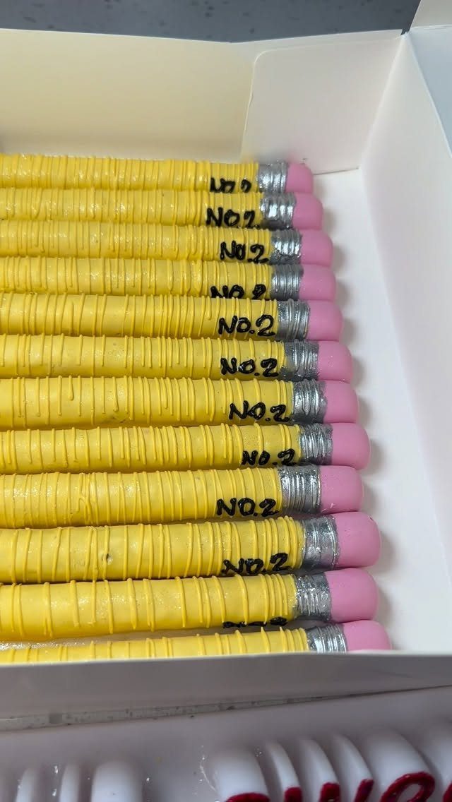 Pencil-shaped yellow treats with pink erasers arranged in a white gift box.