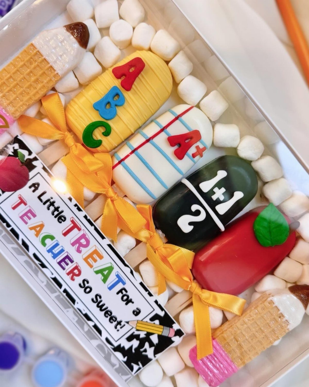 Decorated teacher-themed treats and marshmallows in a white tray with a gift card.