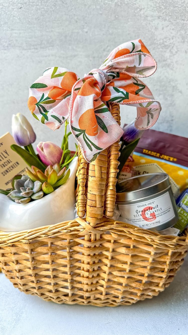 Woven gift basket with a citrus bow, scented candle, sunscreen, and small plants.
