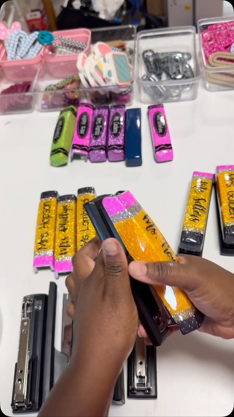 Hands holding a stapler decorated with glitter to look like a pencil.