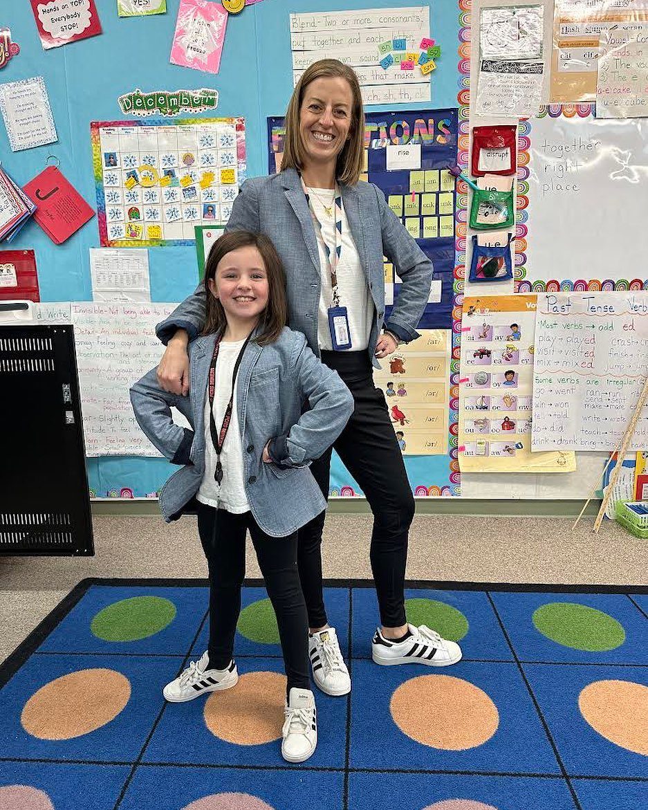 Woman and young girl wearing matching grey blazers and black pants in a classroom.