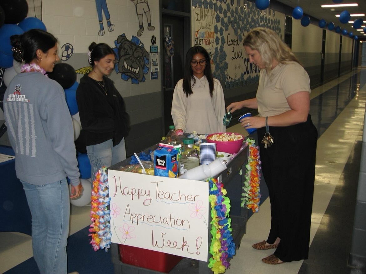 Women gathering around a decorated snack table for Teacher Appreciation Week in a hallway.