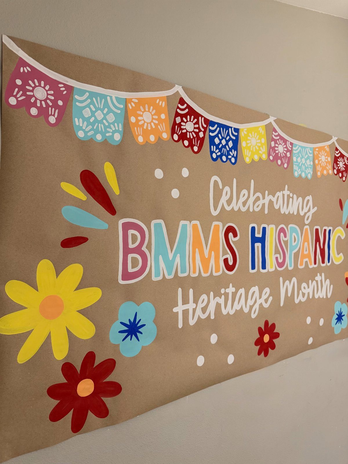 Handmade Hispanic Heritage Month banner on brown paper with colorful flowers and flags.