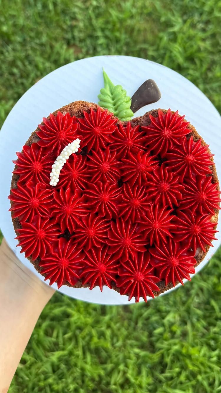 Apple shaped cake with red frosting swirls, a green leaf, and brown stem.