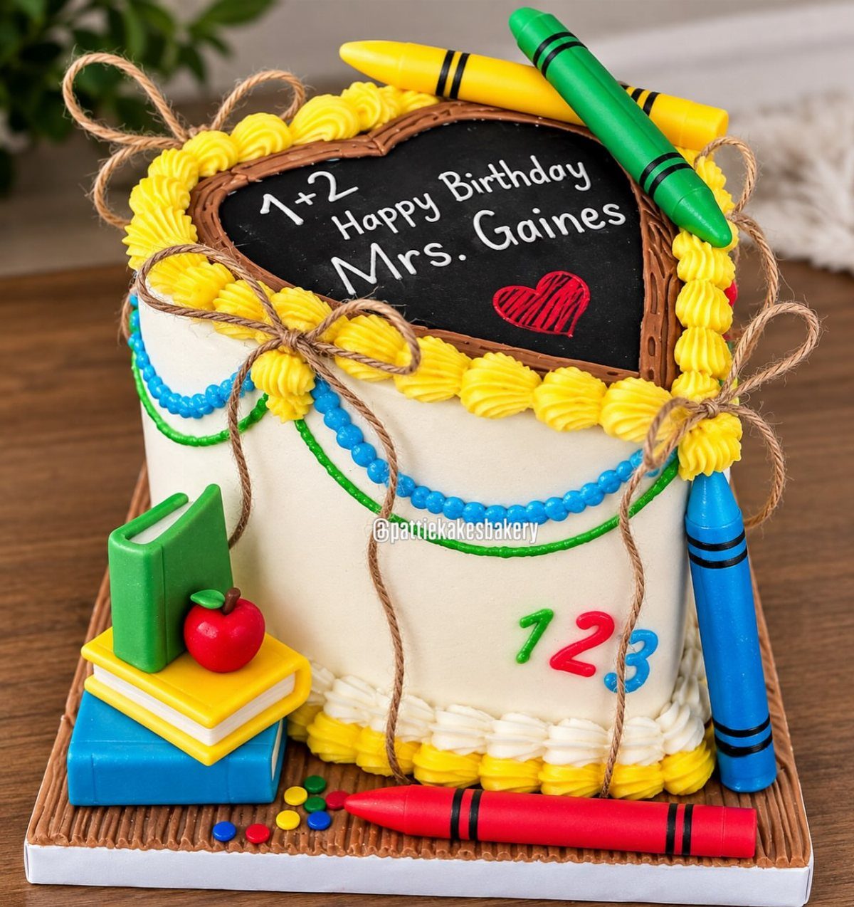 Teacher birthday cake decorated with a chalkboard heart, fondant crayons, and stacked books.