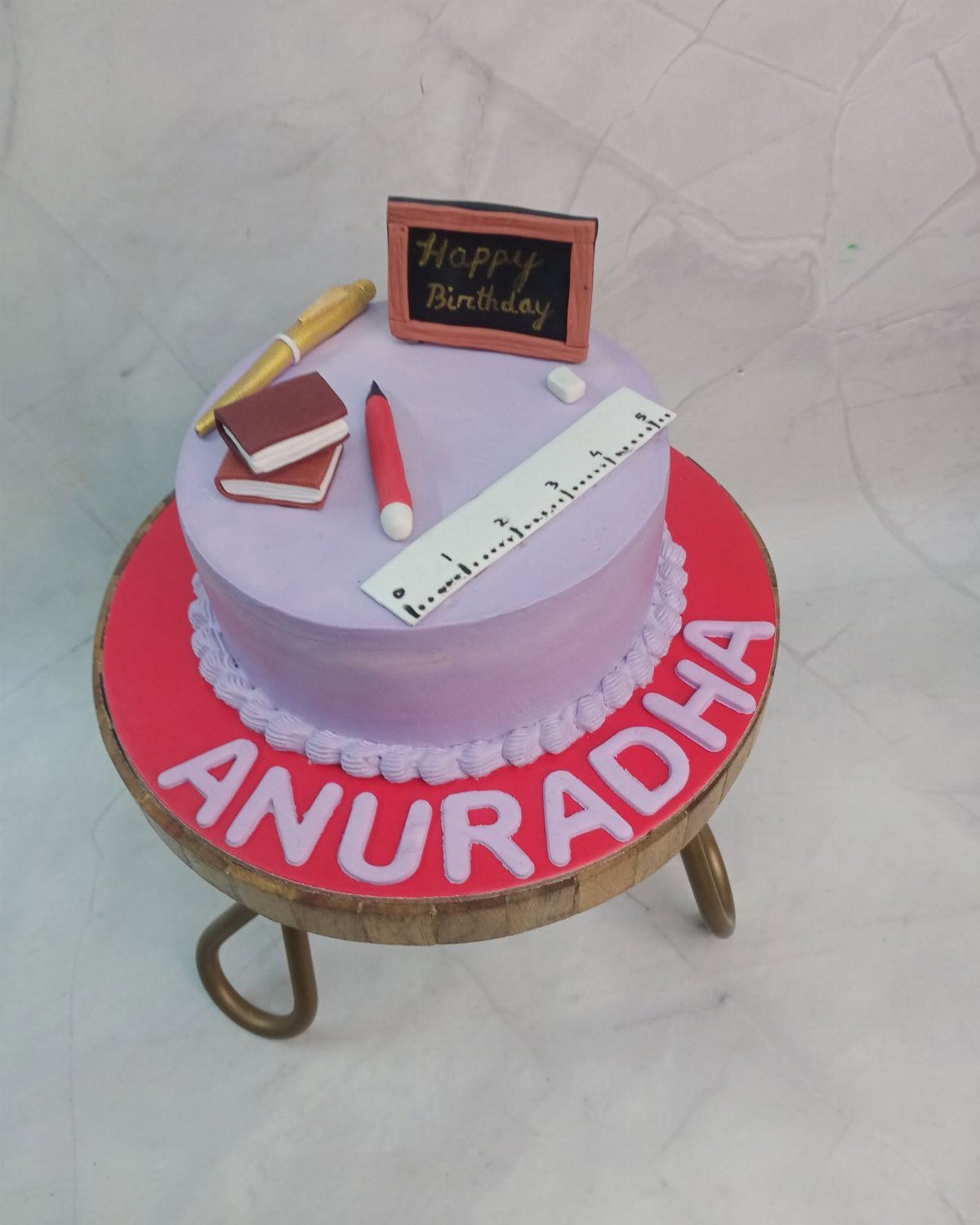 Purple birthday cake decorated with a fondant ruler, pencils, book, and chalkboard.
