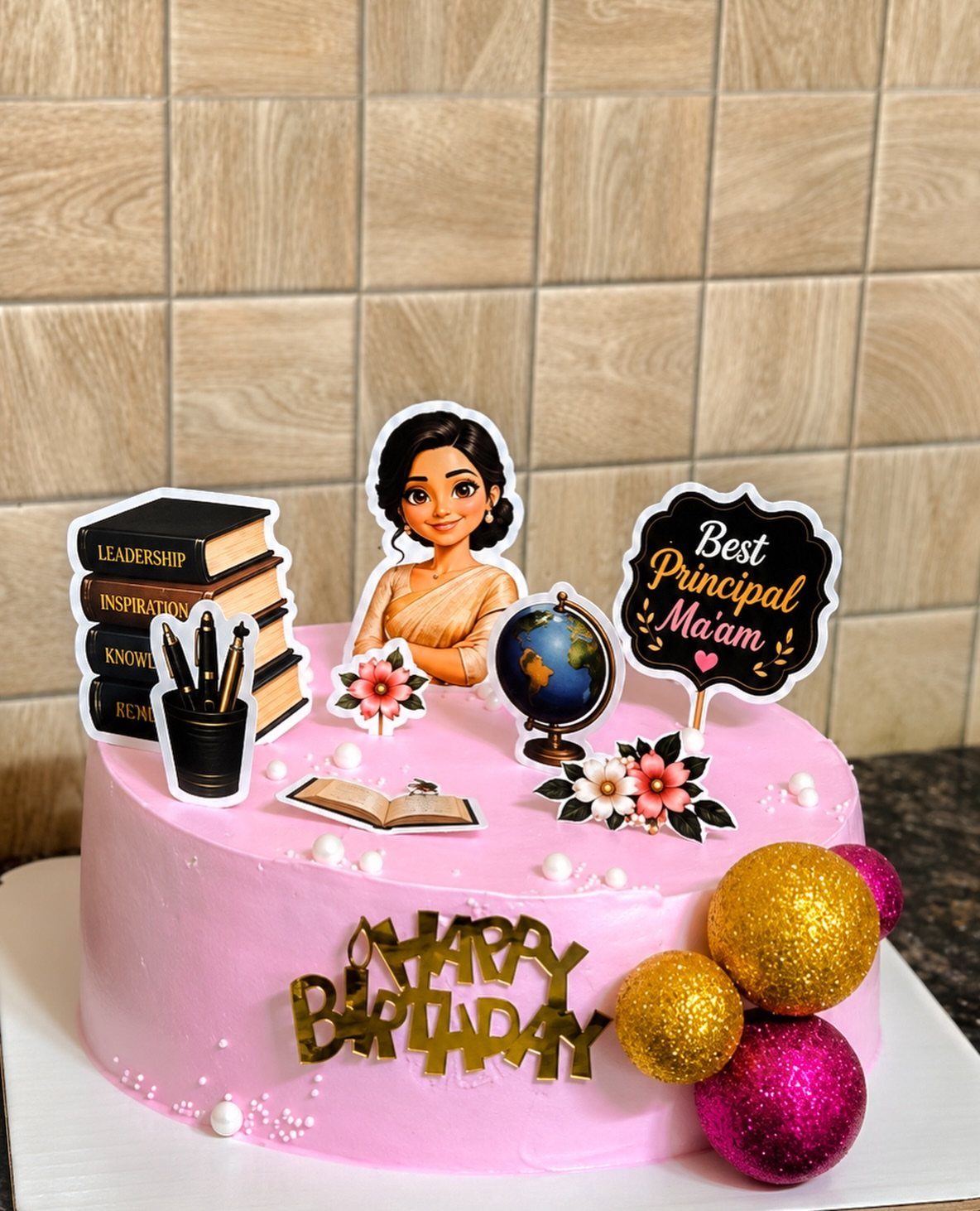 Pink birthday cake with teacher-themed toppers including books, a globe, and a principal sign.