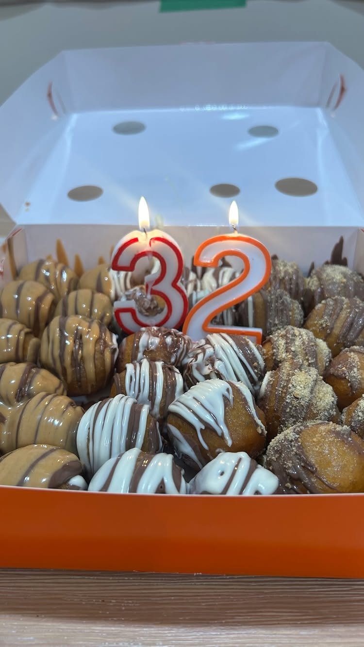 Donut holes in a white box with lit number 32 birthday candles.