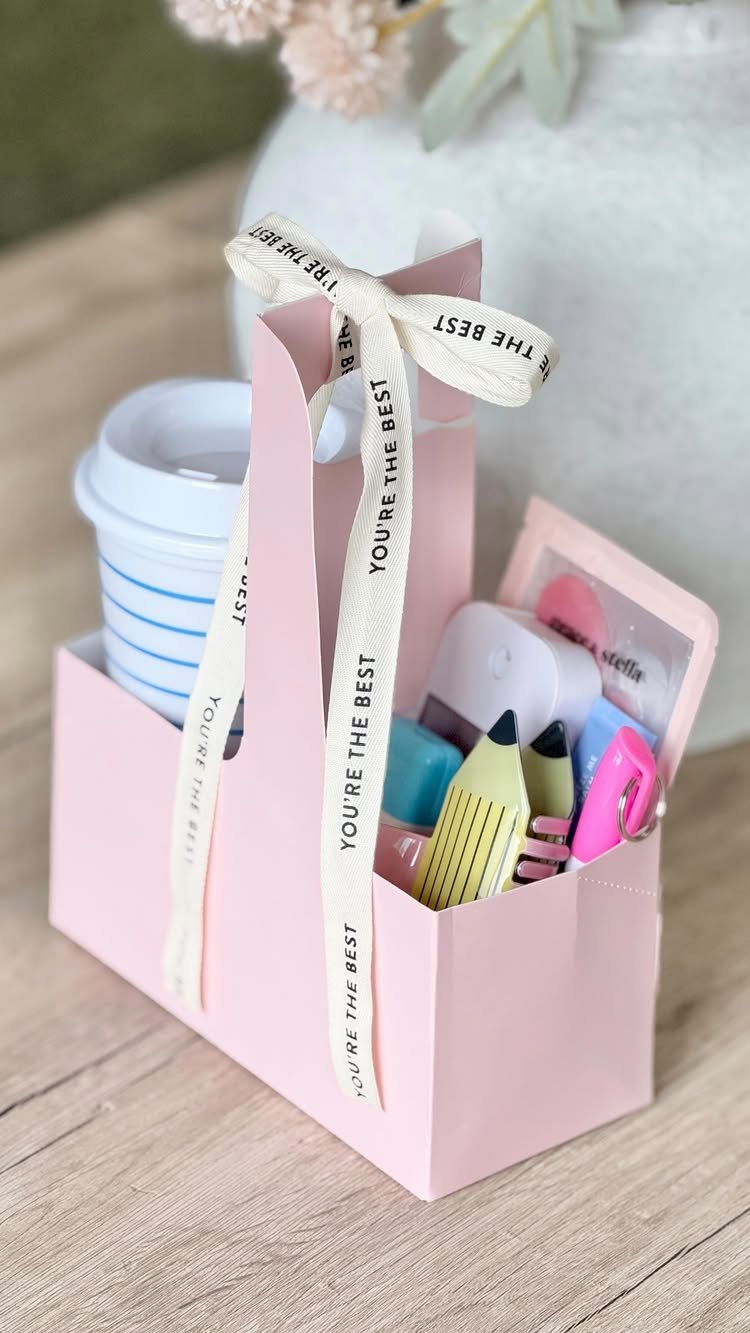 Pink gift bag filled with highlighters, a stapler, and a coffee cup.