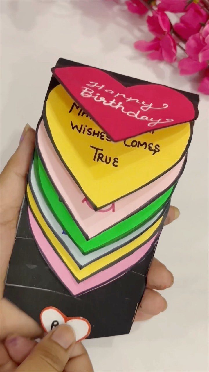 Handmade birthday card with stacked colorful paper hearts held in a person's hand.
