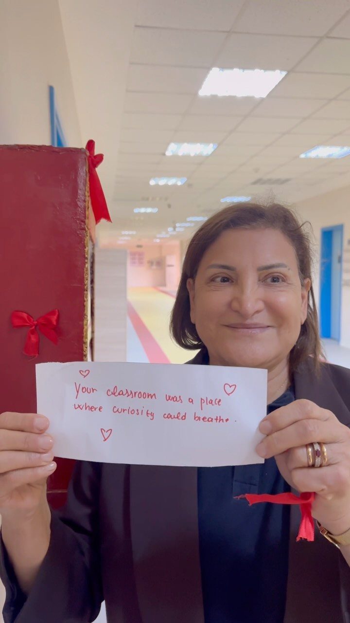 Woman holding a handwritten note with a heartfelt message in a school hallway.