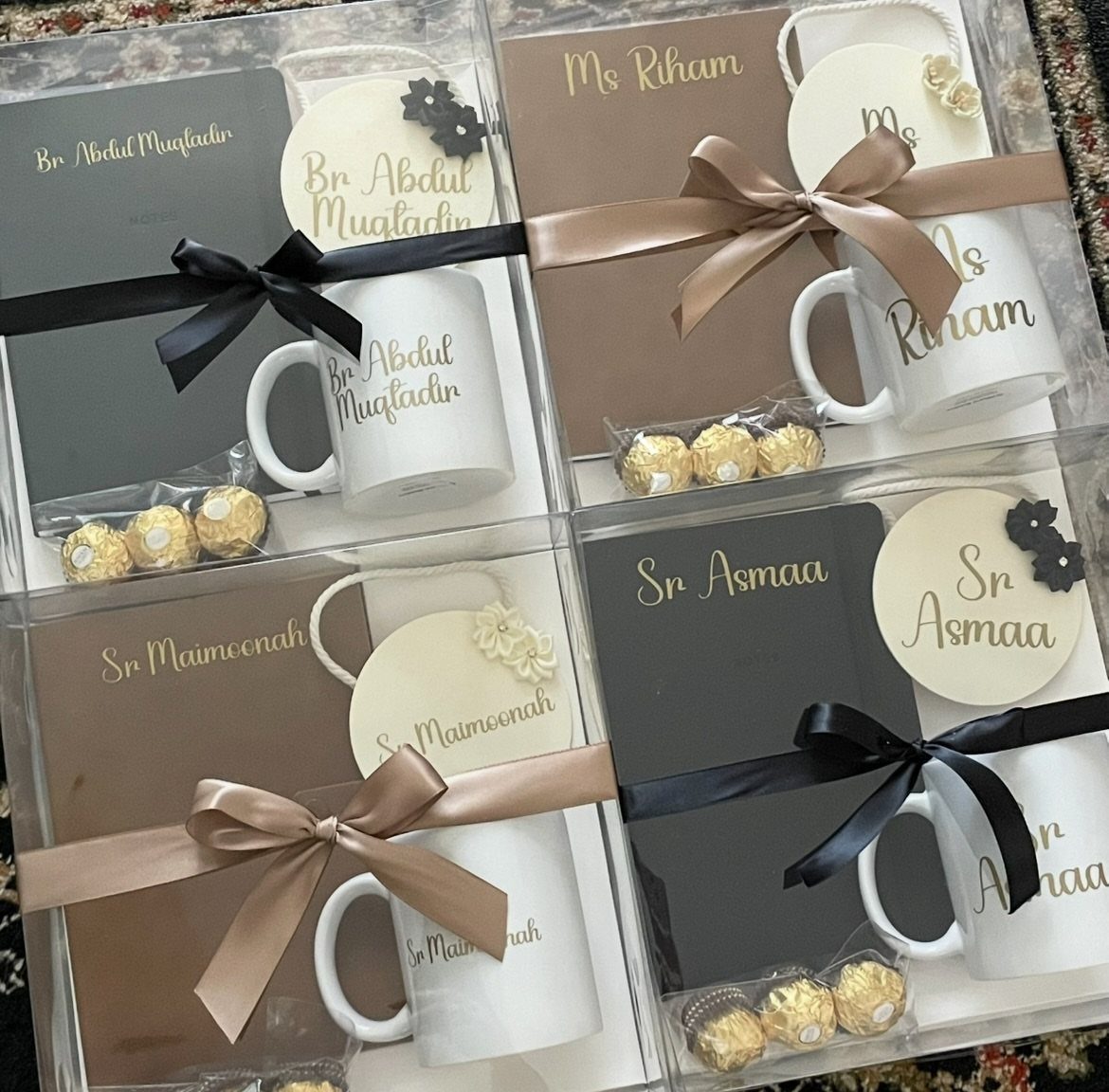 Four personalized gift sets with white mugs, notebooks, and chocolates in clear boxes.