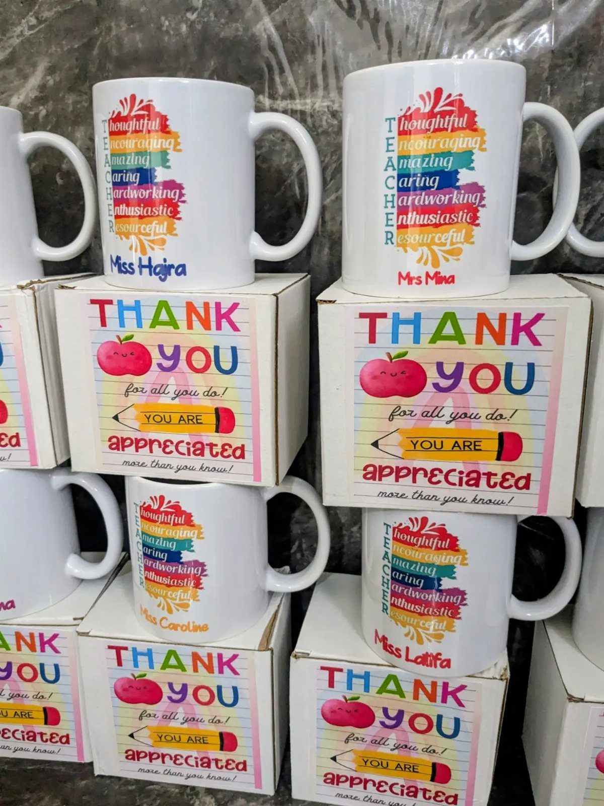 White ceramic mugs with rainbow teacher acrostics on matching thank you boxes.