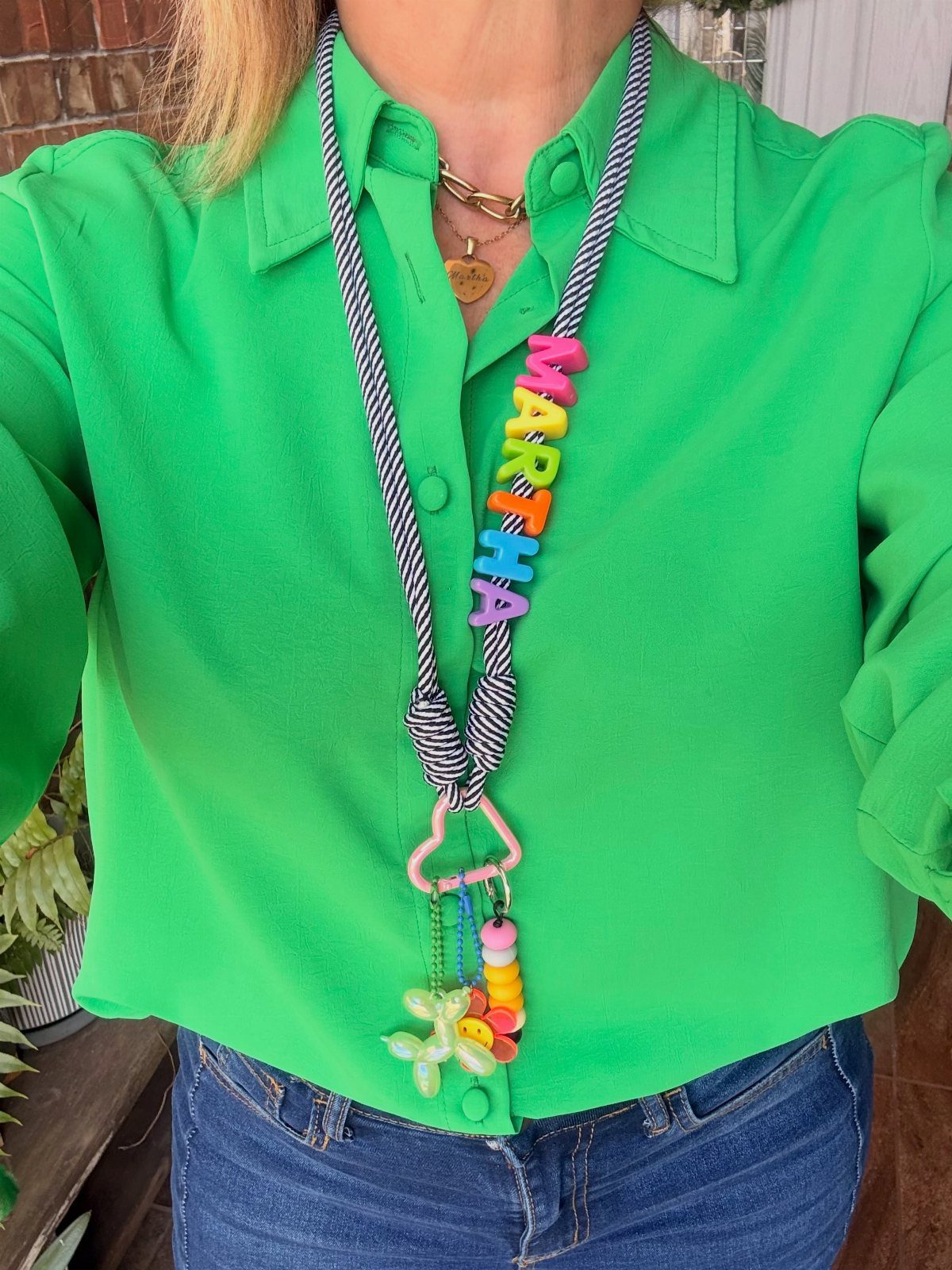 Striped lanyard with colorful letter beads spelling Martha worn over a green shirt.