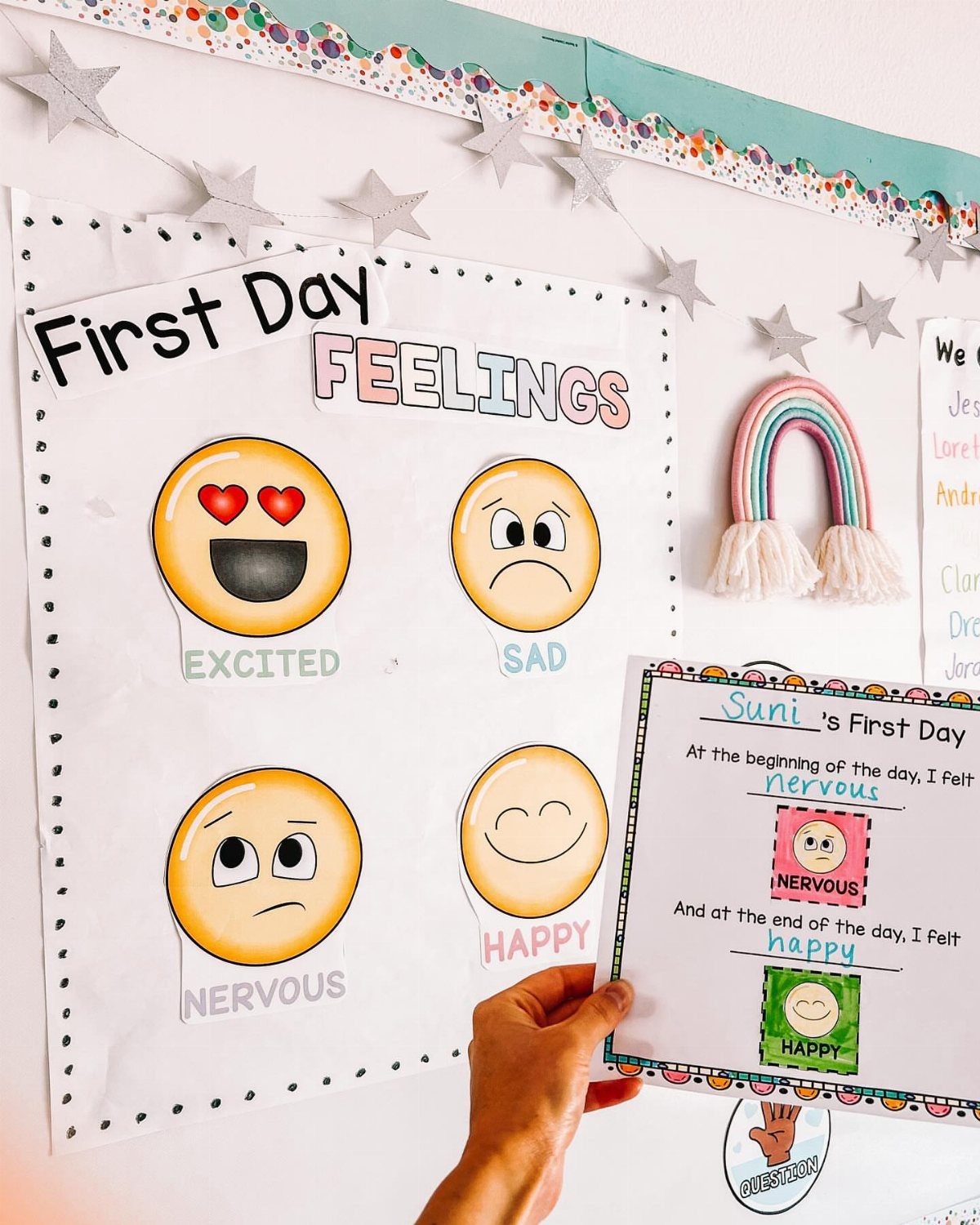 Student feelings worksheet held in front of a first day emotions classroom chart