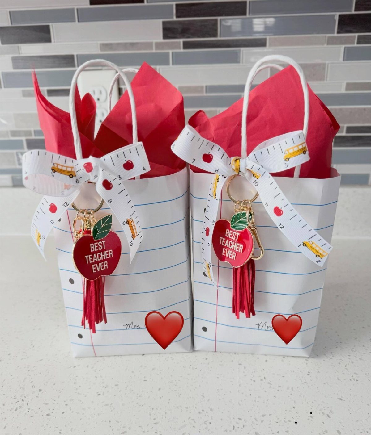 Two teacher gift bags with red tissue paper and apple-shaped keychains.